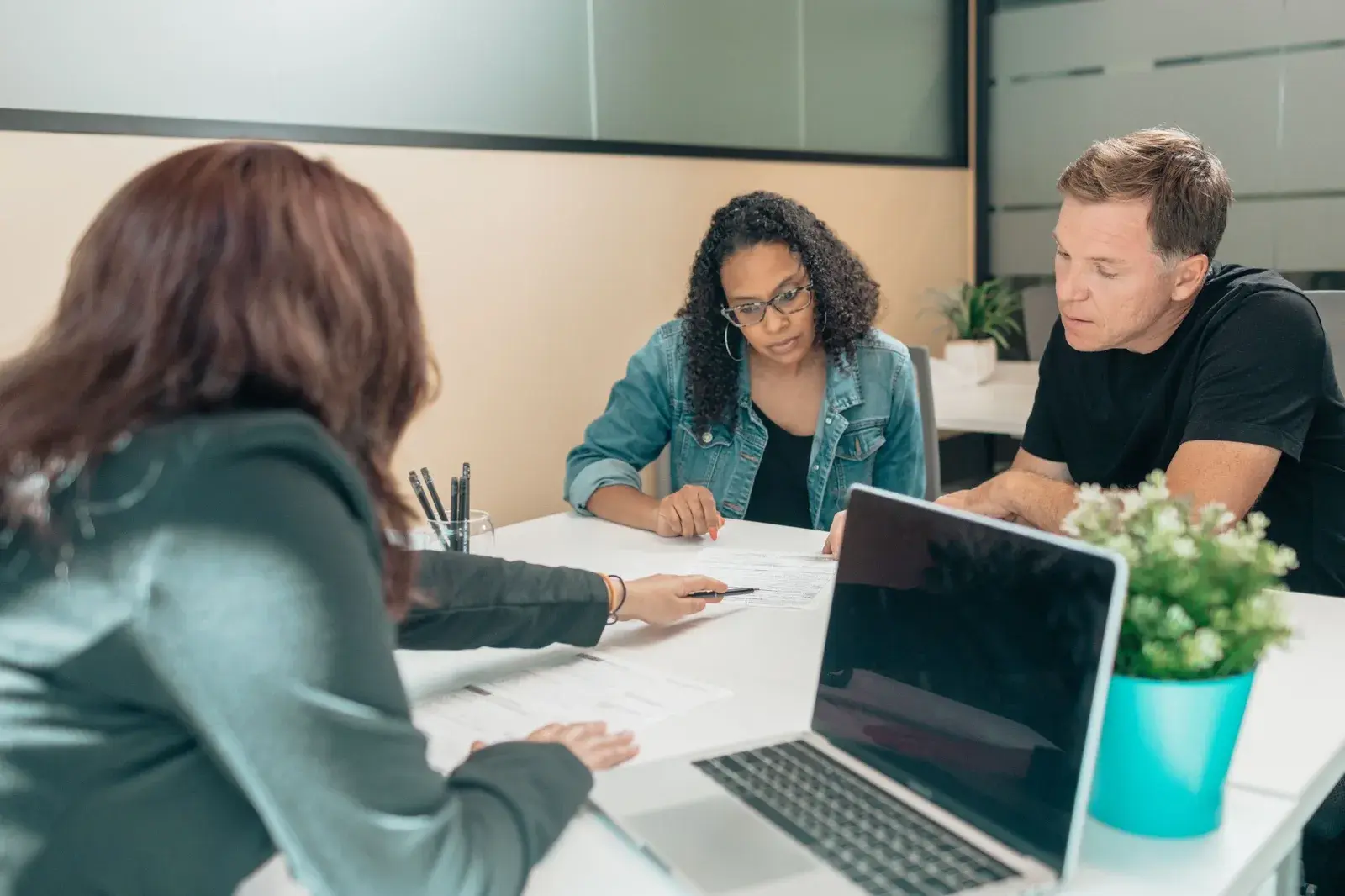 Three people at a meeting table reviewing printed financial forms beside a laptop